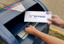 Hands mailing a ballot envelope into a blue mailbox