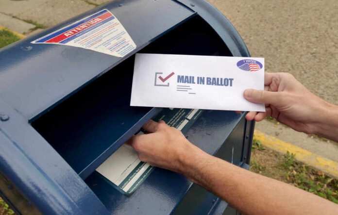 Hands mailing a ballot envelope into a blue mailbox