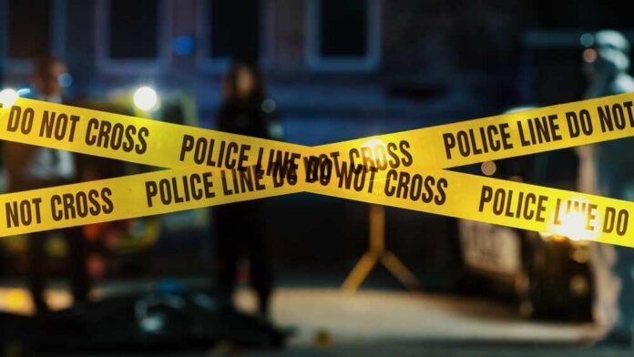 Police tape marking a crime scene with blurred figures in the background