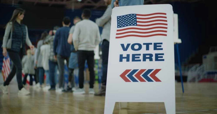 shutterstock_2454758105 People in line next to Vote Here sign