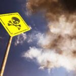 Yellow skull and crossbones warning sign against smoky sky