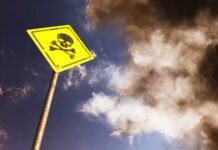 Yellow skull and crossbones warning sign against smoky sky