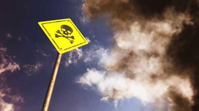 Yellow skull and crossbones warning sign against smoky sky