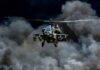 Military Apache helicopter flying through a cloud of smoke