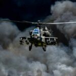 Military Apache helicopter flying through a cloud of smoke