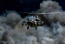 Military Apache helicopter flying through a cloud of smoke