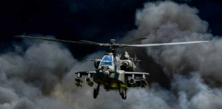 Military Apache helicopter flying through a cloud of smoke