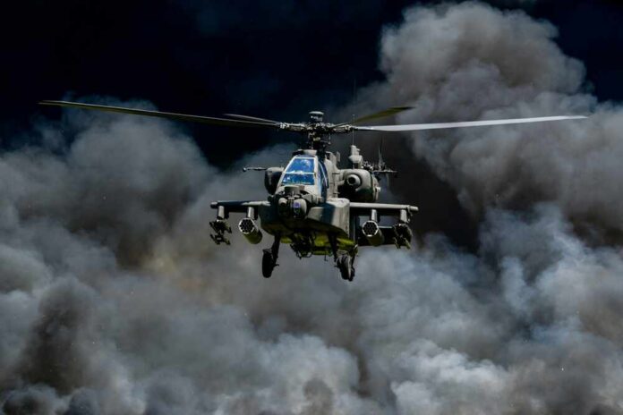 Military Apache helicopter flying through a cloud of smoke