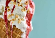 Close-up of an ice cream cone topped with strawberry sauce and chopped nuts