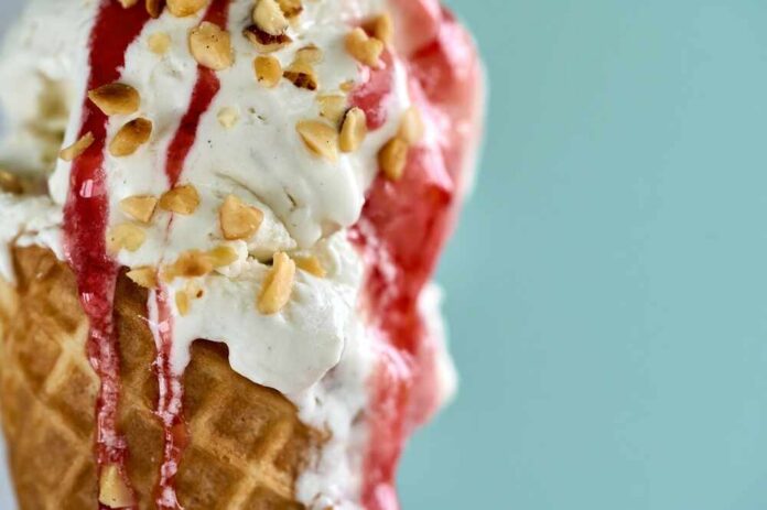 Close-up of an ice cream cone topped with strawberry sauce and chopped nuts