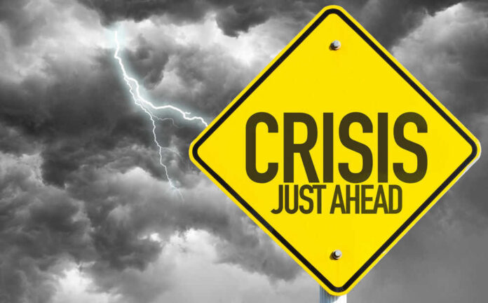 shutterstock_327481232 Yellow sign reading Crisis Just Ahead with stormy sky
