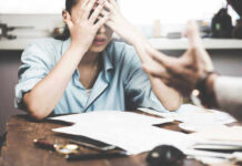 Household Strain Hits Alarming High Stressed woman with hands on face at a desk.
