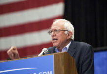 Bernie Sanders speaking at a podium with a U.S. flag backdrop