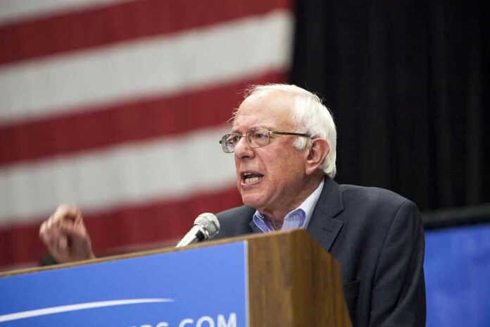 Bernie Sanders speaking at a podium with a U.S. flag backdrop
