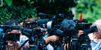 TV news cameras crowding together at an outdoor event
