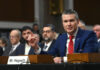 Man in blue suit testifying at a hearing with microphone
