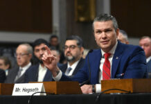 Man in blue suit testifying at a hearing with microphone