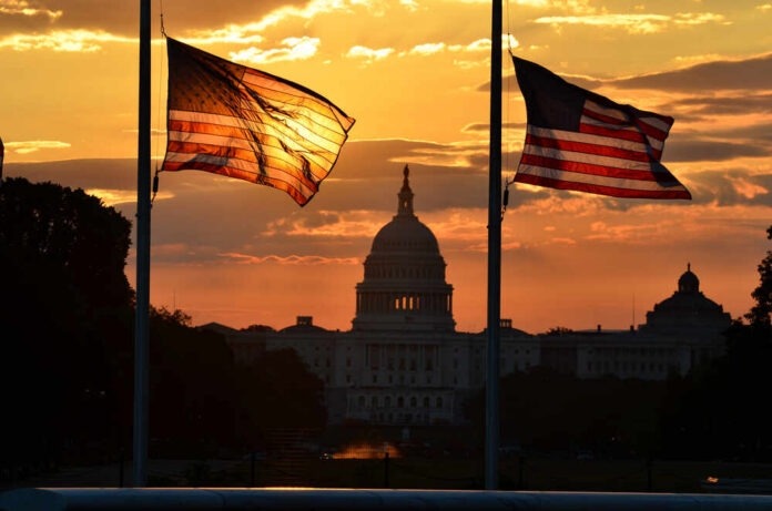 United,States,Capitol,Building,Silhouette,And,Us,Flags,At,Sunrise Silhouetted American flags in front of the Capitol building during sunset