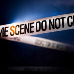Police tape reading 'CRIME SCENE DO NOT CROSS' in a dark setting