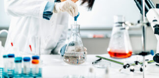 Scientist in a lab using a pipette to transfer liquid into a flask