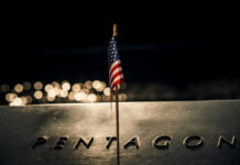 GOP Civil War: Pentagon Boss In The Crosshairs? American flag above engraved Pentagon sign at night
