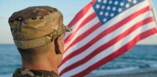 Soldier in uniform standing in front of an American flag by the ocean