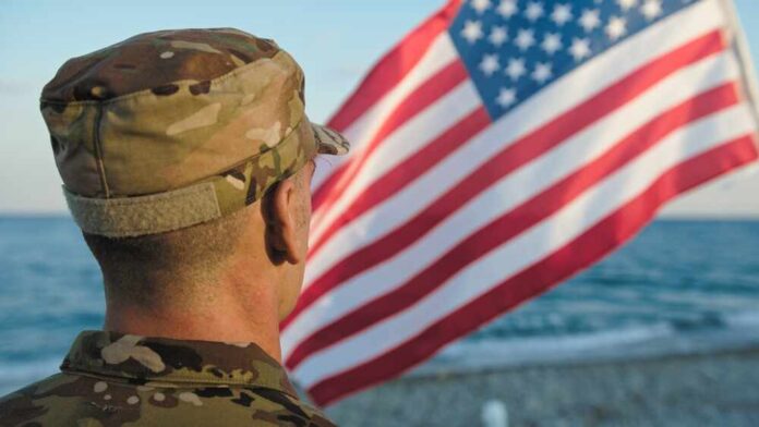 Soldier in uniform standing in front of an American flag by the ocean