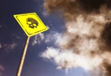 Yellow warning sign with skull symbol under dramatic cloudy sky