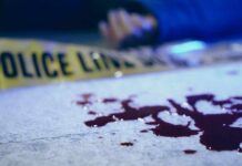 Blood on pavement with police tape and a hand in the background