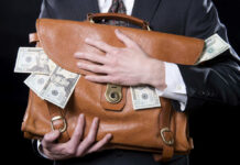 Person clutching leather bag with money sticking out.