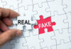 A hand holding a white puzzle piece labeled 'REAL' next to a red puzzle piece labeled 'FAKE'