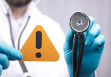 Stockouts Triggered Chaos – Babies Paid First Doctor with stethoscope holding a warning sign