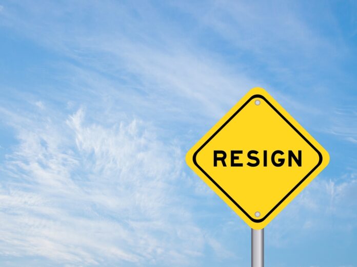 A yellow warning sign with the word 'RESIGN' against a blue sky