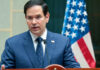 Marco Rubio speaking at a podium with a U.S. flag in the background