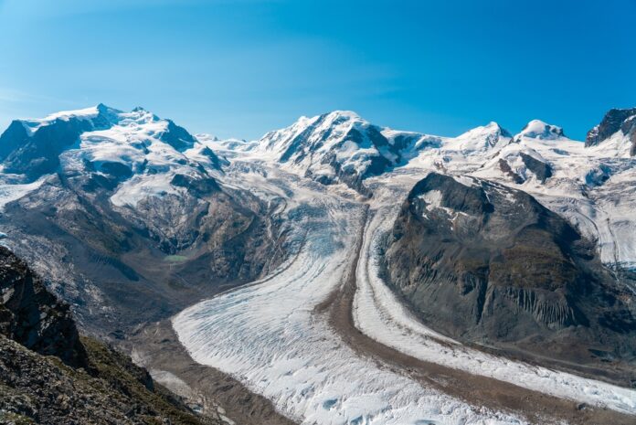 Glacier winding through snow-capped alpine mountains under a clear blue sky