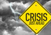 US Orders Exit Over Strikes Yellow sign reading Crisis Just Ahead with stormy sky